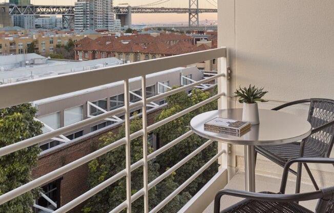 A balcony with a table and chairs overlooking a cityscape.