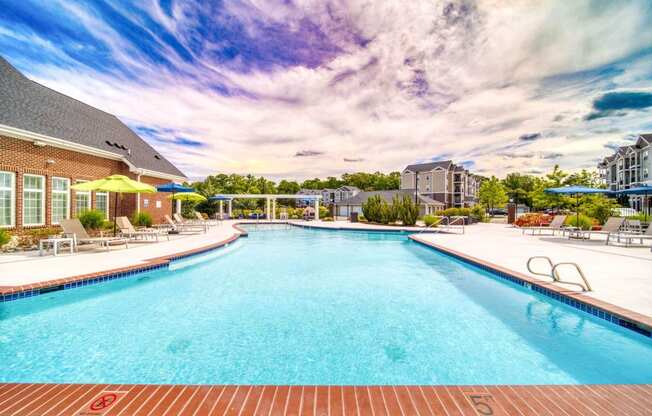 a swimming pool with lounge chairs and umbrellas in front of a brick building at Meridian Obici, Suffolk, 23434