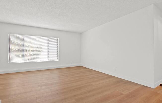 A room with wooden flooring and a window with blinds.