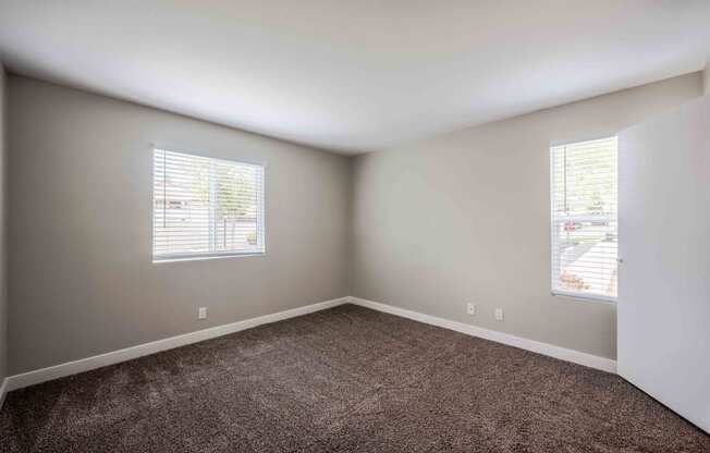 an empty room with carpet and two windows