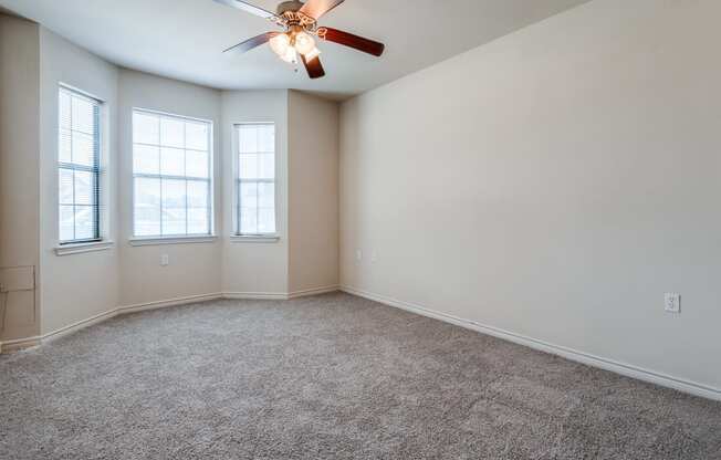 an empty room with a ceiling fan and three windows