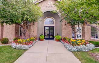 the front of a brick building with flowers and trees