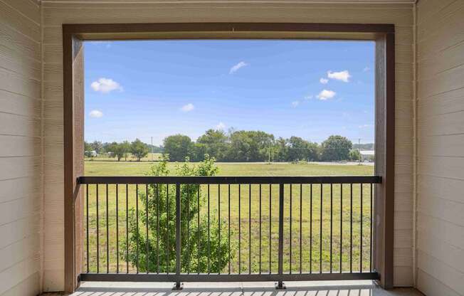 A balcony with a black railing and a view of a green field.