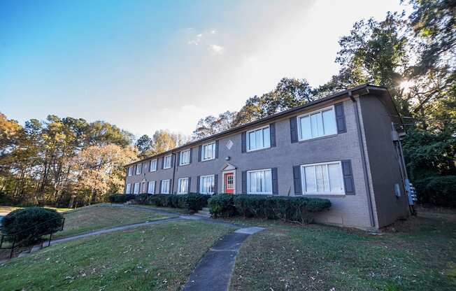 a brick building with a red door on a grassy hill with trees in the background at Broadway at East Atlanta, Atlanta, GA