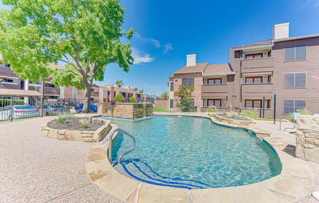 A swimming pool surrounded by a stone patio and a tree.