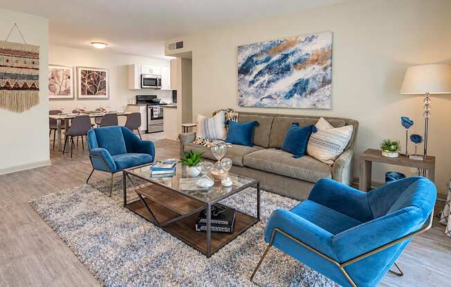 Furnished living room with a sofa and blue accent chairs, opening to the dining area and kitchen at Icon Avondale Apartments in Decatur, GA.