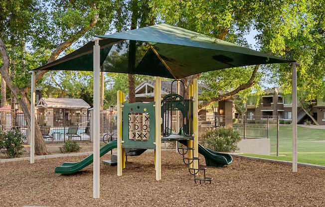 A playground with a green slide and a canopy.