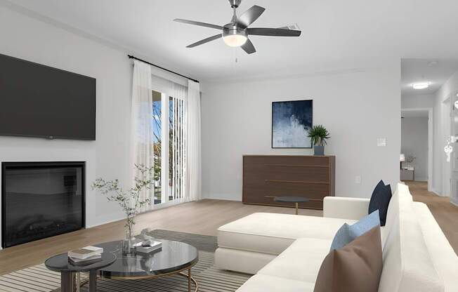 A modern living room with a white sofa, a coffee table, a flat screen TV, and a ceiling fan.