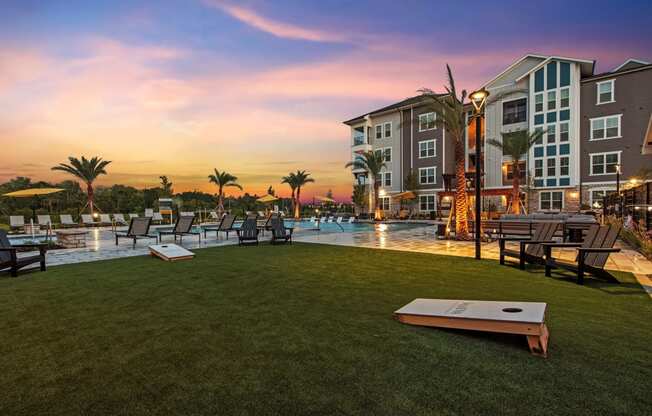a swimming pool with lounge chairs and tables and a sunset in the background