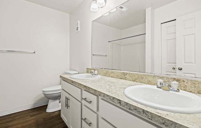 A bathroom with a toilet, two sinks, and mirror at Tanglewood Apartments, Oak Creek, WI