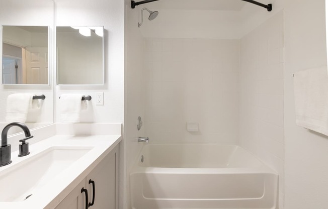 A white bathroom with a tub, sink, and mirror.