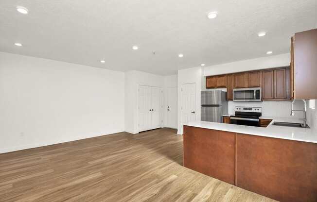 an empty living room and kitchen with wood flooring and white walls