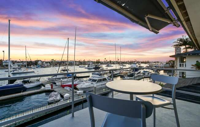 a view of a marina at sunset from a balcony with a table and chairs