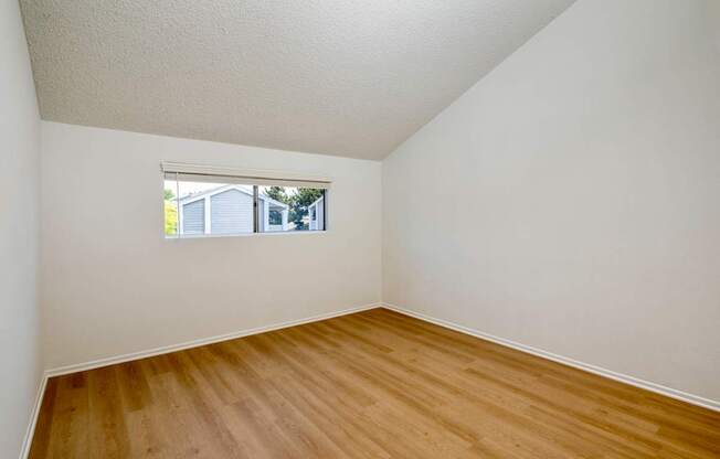 A bedroom with hardwood floors and a window.