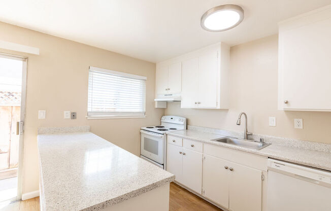 a kitchen with white counters and appliances and a window