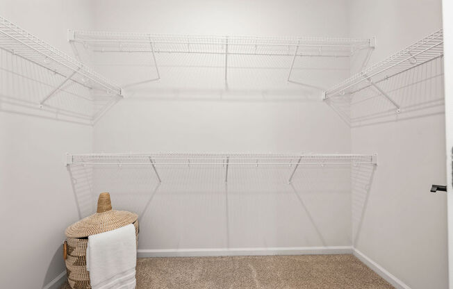 a walk in closet with white walls and shelves and a basket on the floor