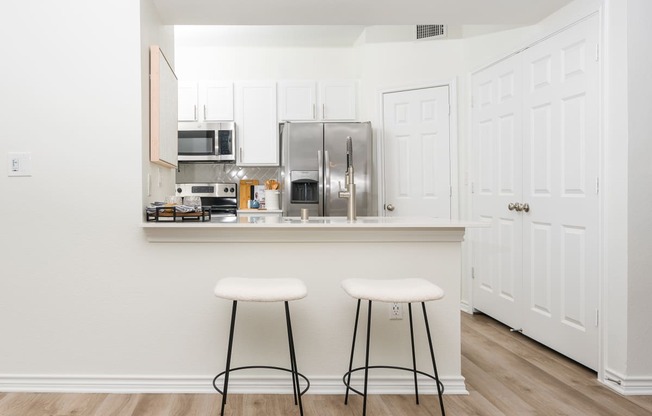 a kitchen with white cabinets and a counter with two stools