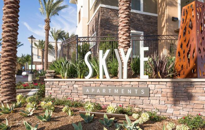 the entrance to the sky apartments sign in front of a brick retaining wall with plants