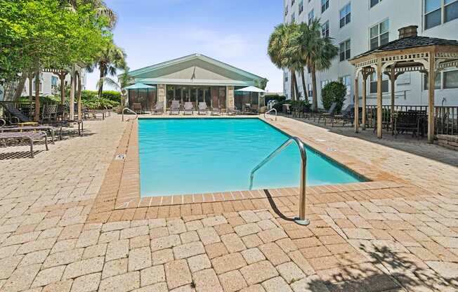 A large swimming pool surrounded by a brick patio and a gazebo in the background.