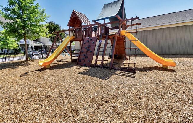 Gated playground with wood chips on the ground near trees and apartment complexes