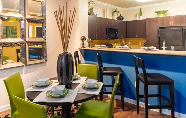 a dining area with a table and chairs and a kitchen in the background