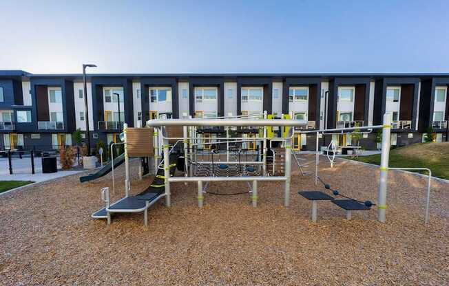 A playground with a slide, swings, and a bench in front of a building.