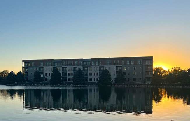 a building on the lake at sunset with the sun setting behind it