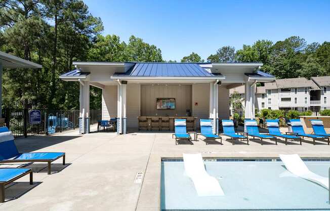 A pool pavilion with a blue roof and white walls is surrounded by blue lounge chairs.
