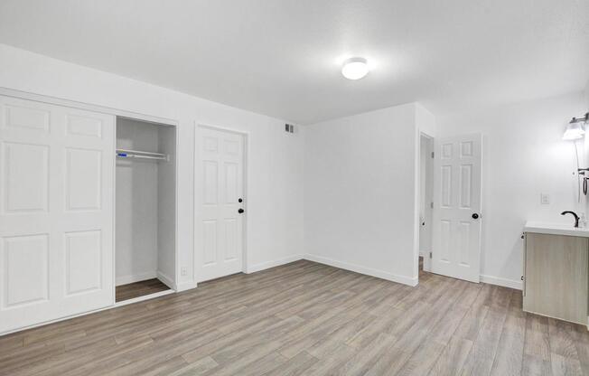 A room with white walls and wooden flooring, featuring a door, a window, and a light fixture.