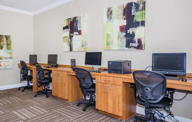two desks with computers and chairs in a room with paintings