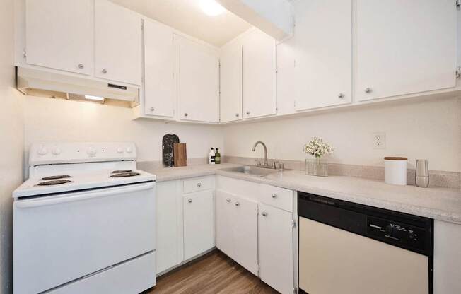 A white kitchen with a stove, sink, and cabinets.