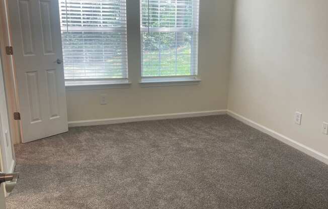 a carpeted room with two windows and a door