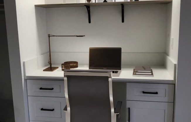 A white desk with a laptop and a chair in front of it.