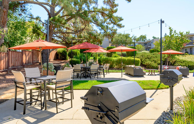 a patio with tables chairs and umbrellas and a grill