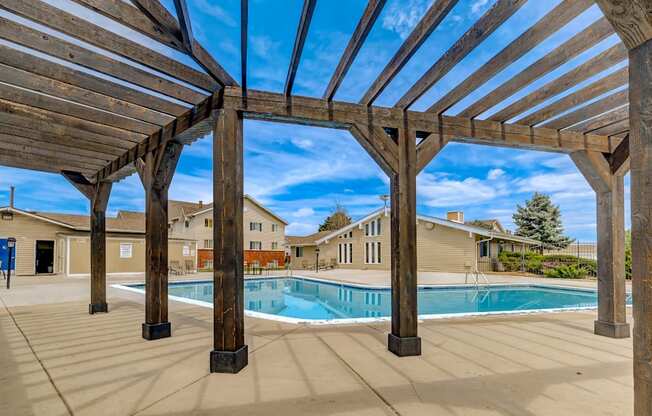 Poolside pergola seating area with apartment buildings in background at Aurora Meadows.