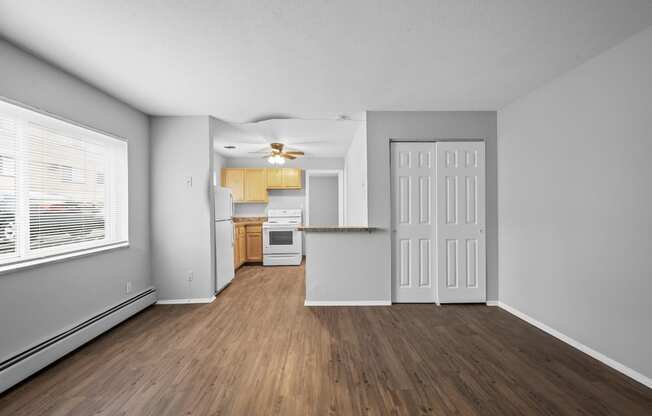 the living room and kitchen of an apartment with wood flooring and a large window