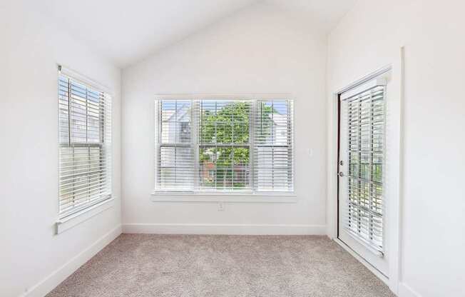 A sun room with a carpeted floor and a windows with blinds.