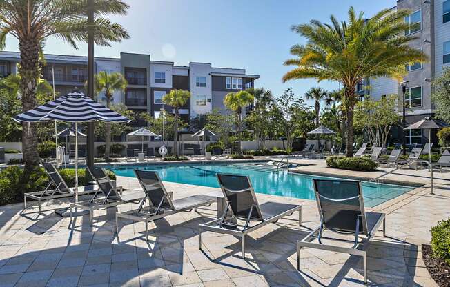 a swimming pool with lounge chairs and umbrellas in front of an apartment building