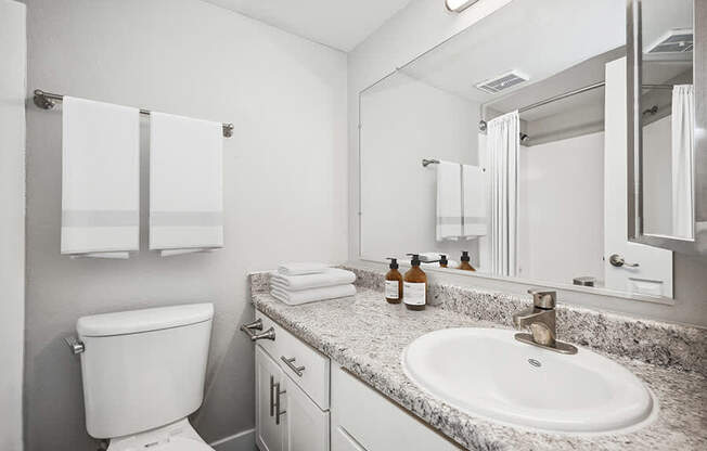 Model Bathroom with White Cabinets and Wood-Style Flooring at Stillwater Apartments located in Glendale, AZ.