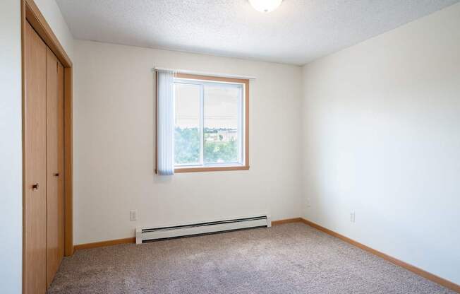 A room with a window and a carpeted floor. Bismarck, ND Sierra Ridge Apartments