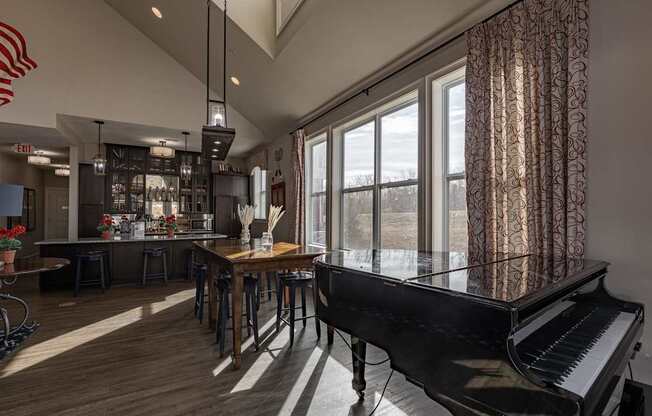 Elegant clubhouse at Queens Gate Apartments featuring natural light, a grand piano, communal dining tables, and a modern bar area.