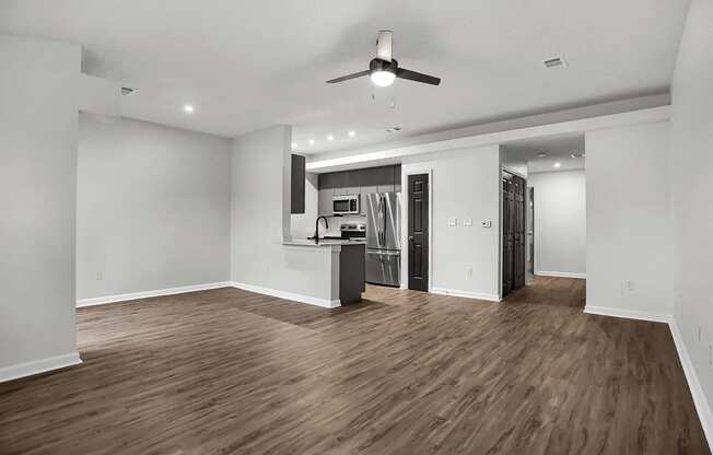 an empty living room with a kitchen and a ceiling fan