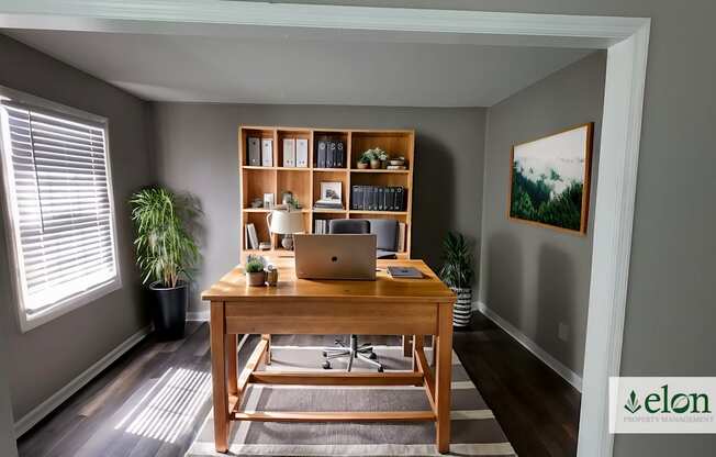 A room with a desk, laptop, and a potted plant.