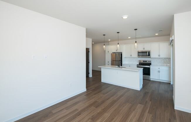 an empty living room with a kitchen with white walls and wood floors at The Crossings at Windsong, Prescott Valley, AZ