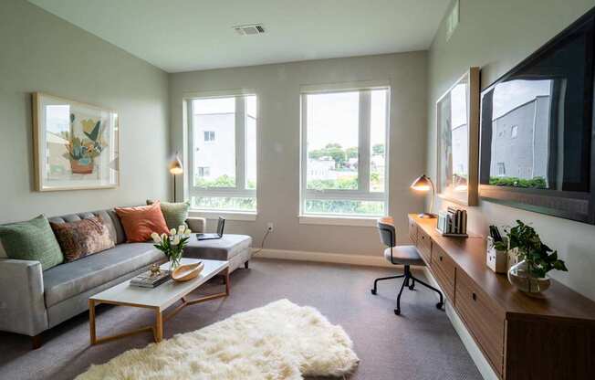 A bedroom setup with a desk area featuring large windows that allow natural light to brighten the room.