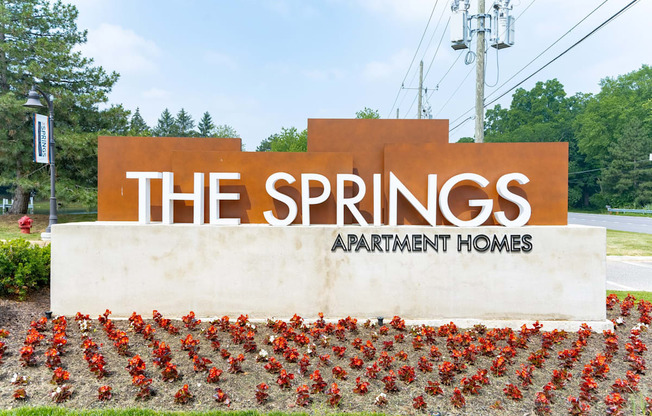 a sign for the springs apartment homes with red flowers in front of it at The Springs Apartment Homes, Michigan