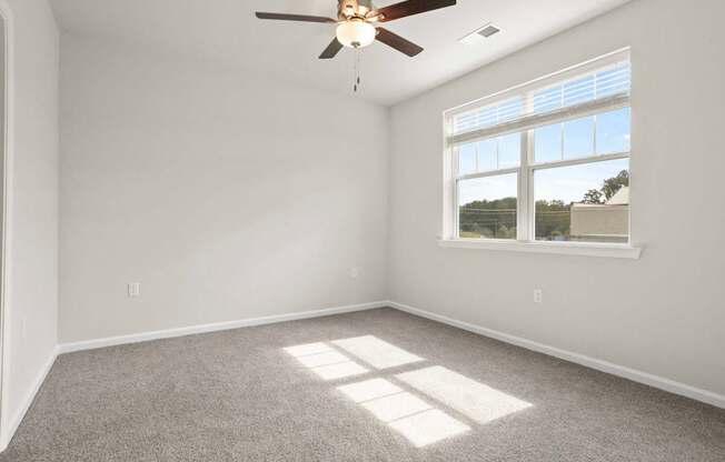 A room with a ceiling fan and a window letting in sunlight.