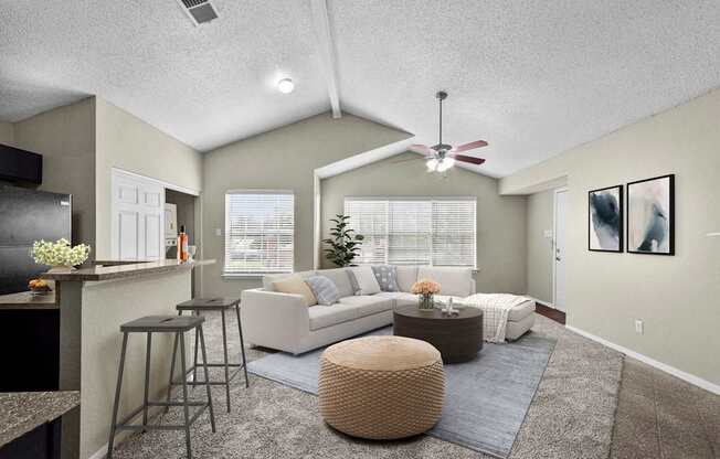 A living room with a white couch, a brown ottoman, and a ceiling fan.