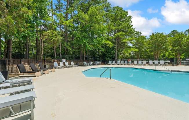 A pool surrounded by trees and lounge chairs.
