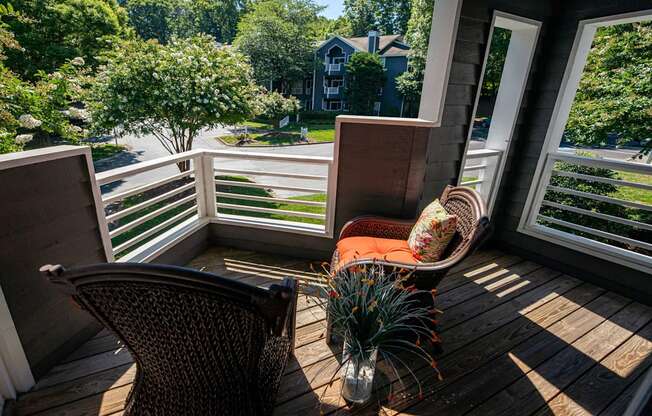 A chair is on a wooden deck with a view of a street and houses.